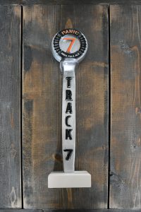 Track 7 Panic India Pale Ale tap handle decal on wooden desk.