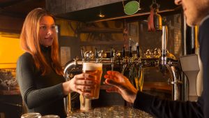 Woman serving craft beer to a customer at a bar.